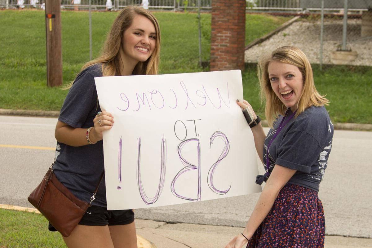two girls hold poster board sign that says welcome to S-B-U